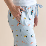 Model showing pockets of blue Women's Lounge Pants in Sushi print under white camisole on a beige background