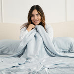 Female sitting in a bed under the Bamboo Sateen Sheet Set in Ice