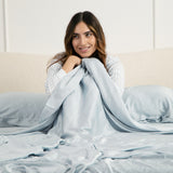 Female sitting in a bed under the Bamboo Sateen Sheet Set in Ice
