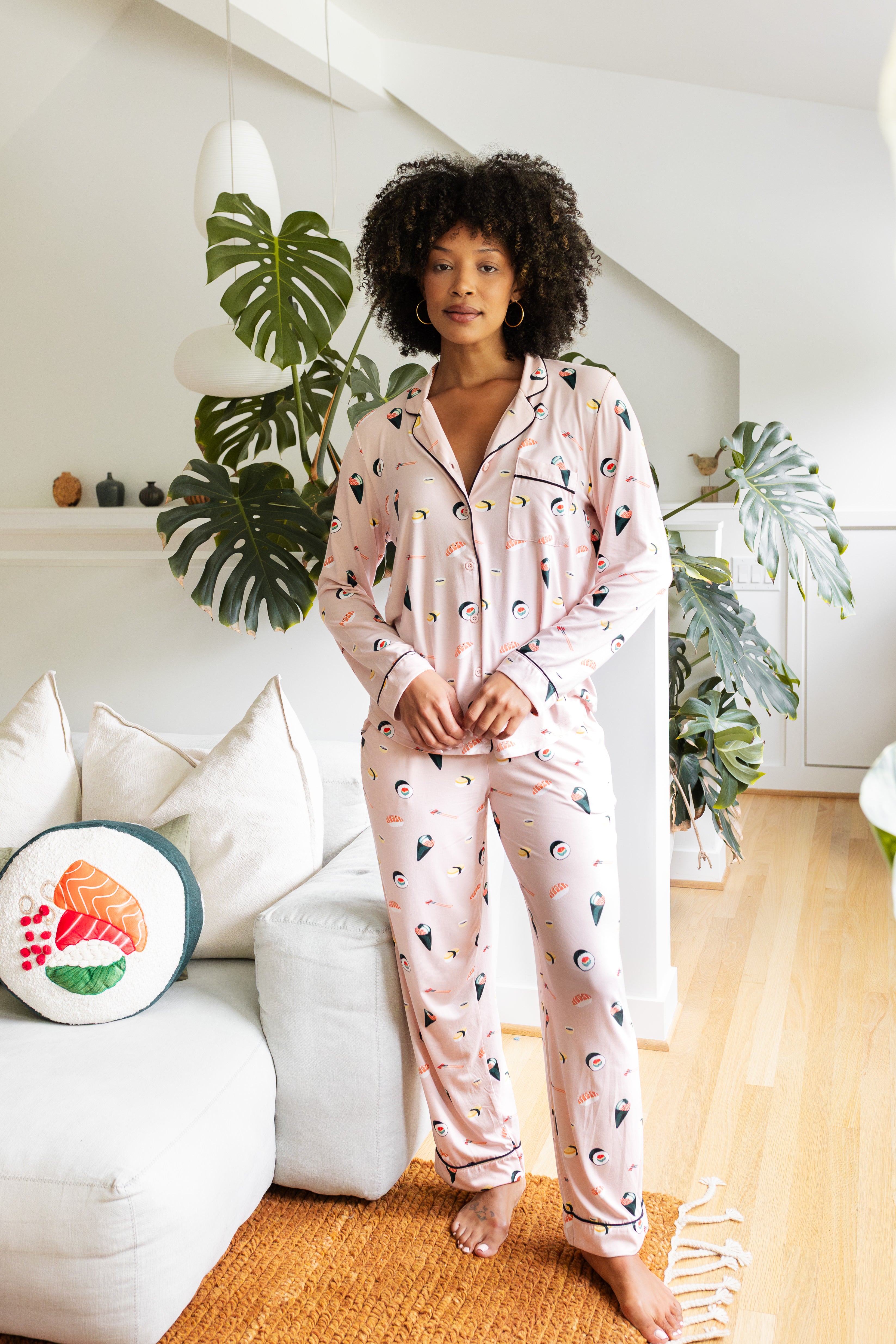 Woman wearing a pink pajama set with a sushi pattern in a living room. ::: Model is 5'9"" wearing size S ///
---1605 3