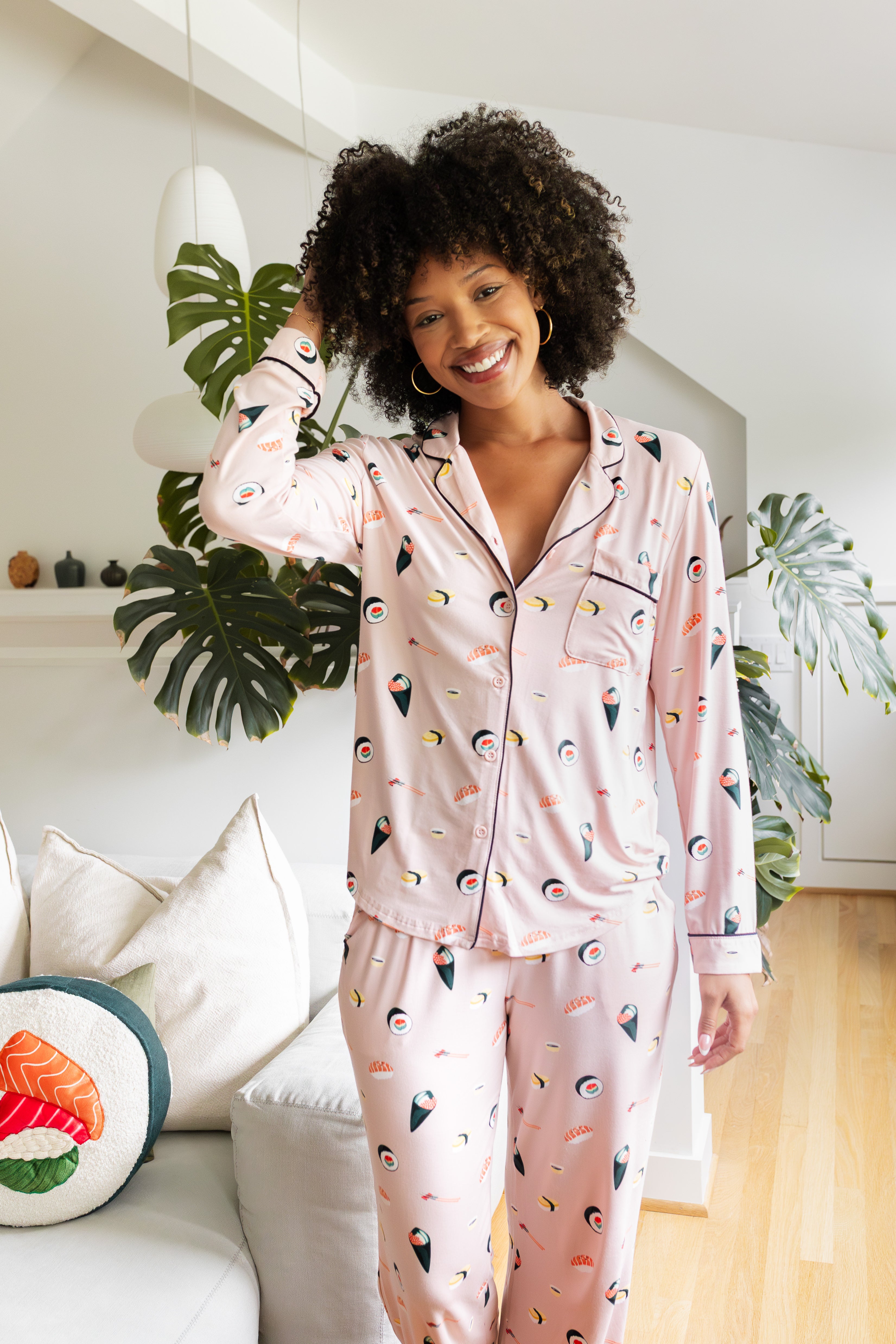 Woman wearing a pink pajama set with sushi print in a cozy living room.
---PJ 4