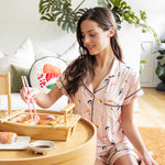 Woman in pink sushi themed pajamas sitting on the floor with a tray of food in a cozy room.
---PJ 2