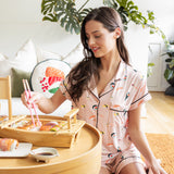 Woman in pink sushi themed pajamas sitting on the floor with a tray of food in a cozy room.
---PJ 2
