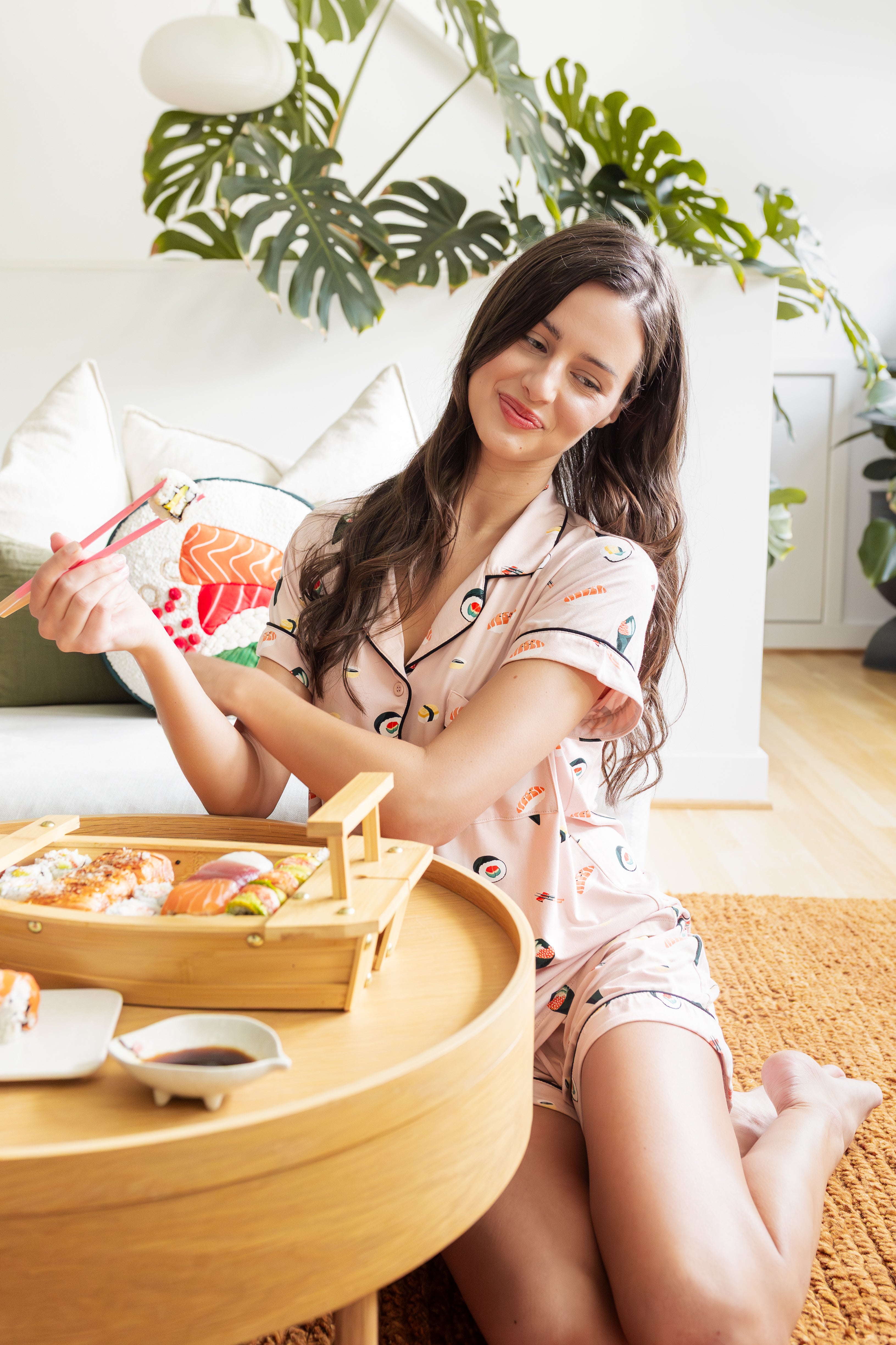 Woman in pajamas enjoying a meal of sushi in a cozy living room.