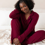 Woman wearing burgundy button up pajamas on a bed with cream colored bamboo bedding  ::: Model is 5'6" wearing size M ///
---1605 1
