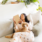 Woman wearing Long-Sleeved Women's Pajama Set in Dachshund reading a book to her blonde dachshund  on a couch with plants in the background

---1605 3
