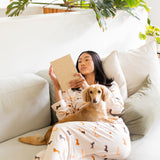 Woman wearing Long-Sleeved Women's Pajama Set in Dachshund reading a book to her blonde dachshund  on a couch with plants in the background

---1605 3