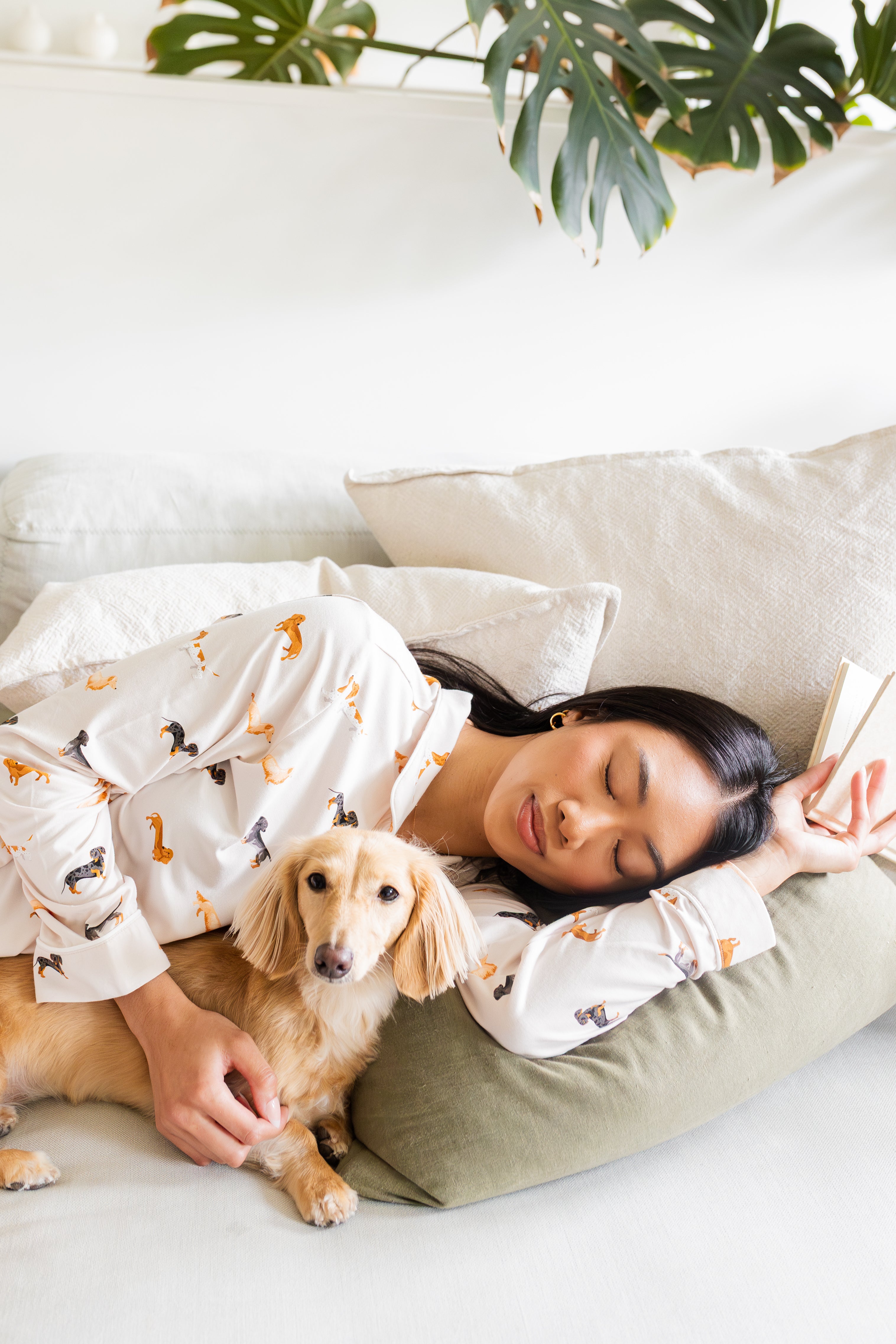 Sleeping model wearing the Long-Sleeved Women's Pajama Set in Dachshund while snuggled with a blonde dachshund 