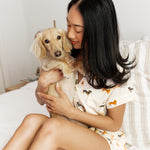 Model snuggling blonde Dachshund while sitting on a bed and wearing the Kyte Women's Short Sleeve Pajama Set in Dachshund