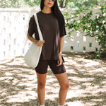 Woman in brown outfit with white sneakers holding a white bag outdoors.