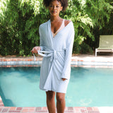 Woman in a light blue robe standing by a pool with greenery in the background