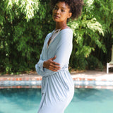 Woman in a light blue robe standing by a pool with greenery in the background