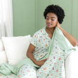 Woman wrapped in a light green blanket with harry potter characters, sitting on a white couch against a green wall.