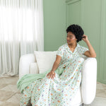 Woman in a harry potter honeydukes patterned pajama sitting on a white chair in a room with green walls and white curtains.