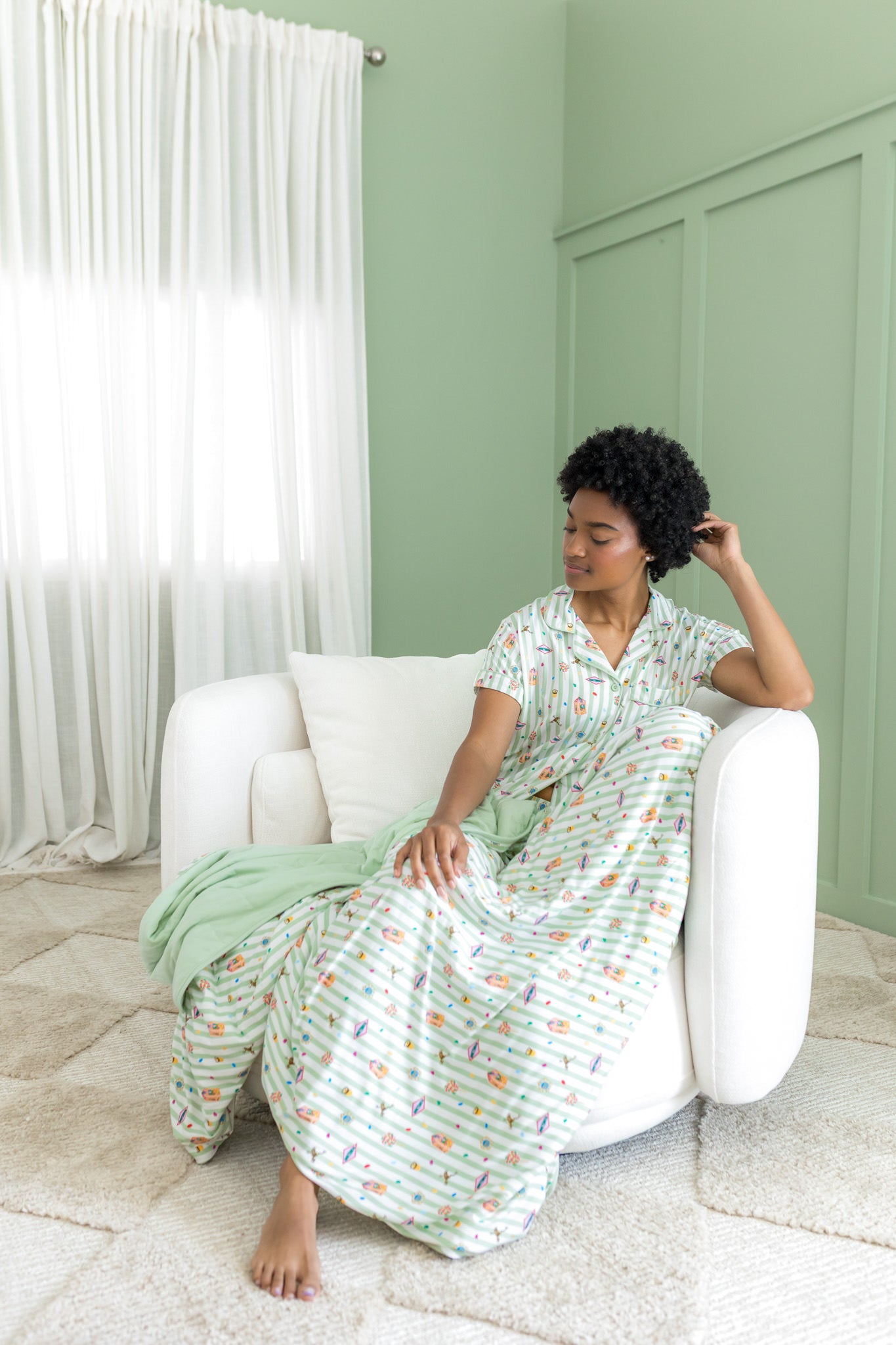 Woman in a harry potter honeydukes patterned pajama sitting on a white chair in a room with green walls and white curtains.