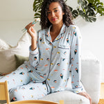 Woman wearing a sushi-themed blue pajama set sitting on a couch with a small bamboo basket of sushi.
---1605 1