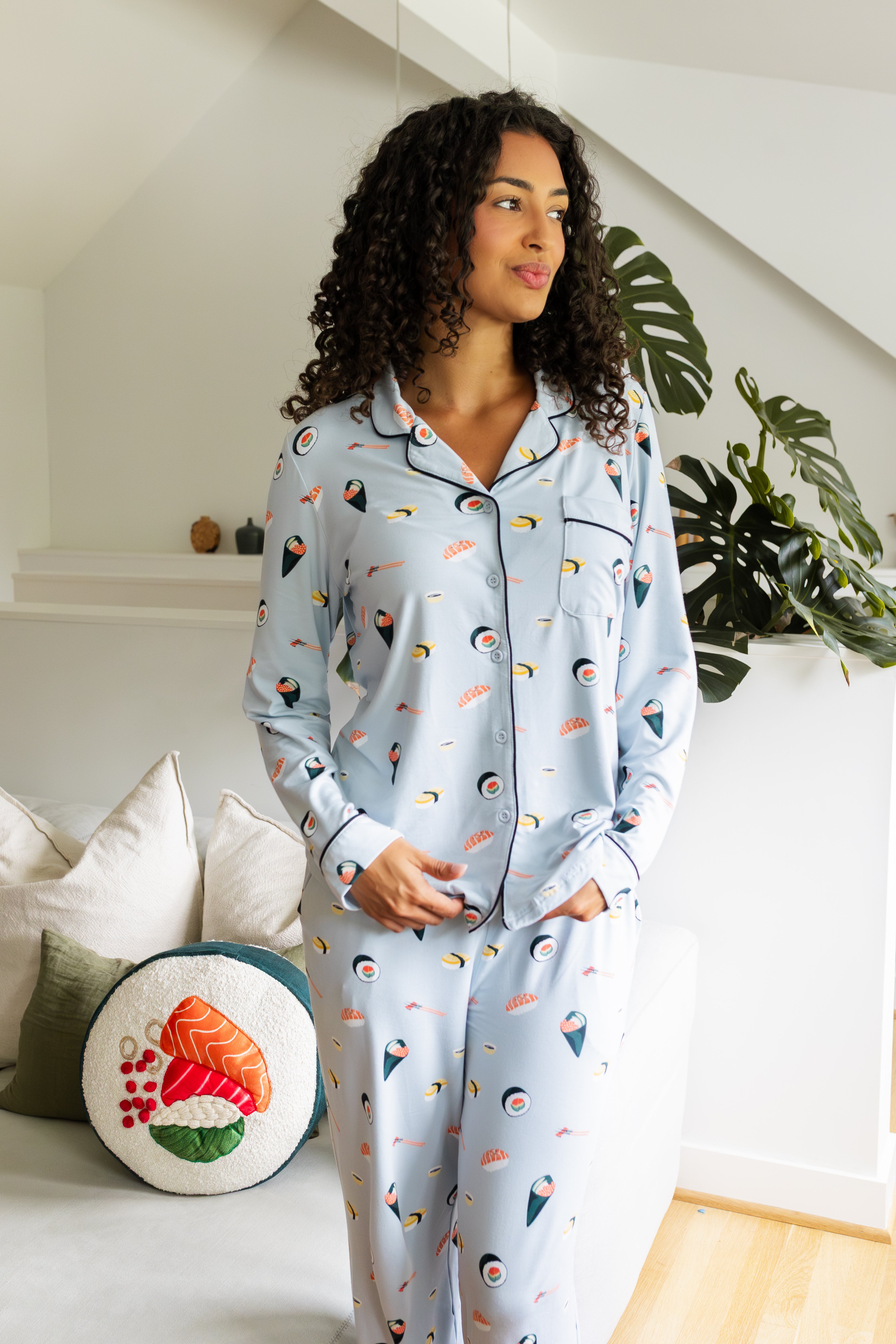 Woman wearing a light blue pajama set with colorful sushi patterns in a cozy living room.
---PJ 2