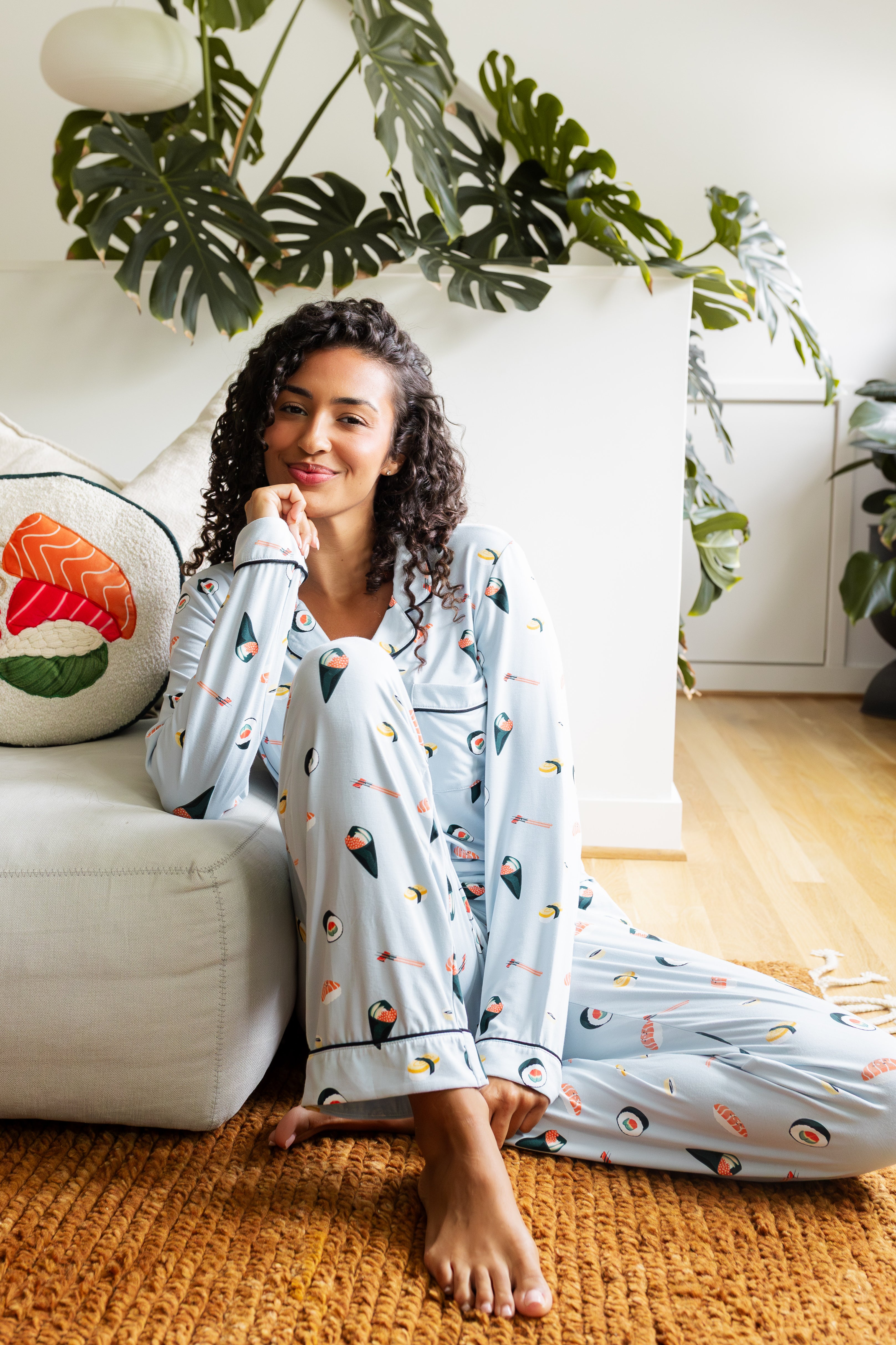 Woman in sushi pajama sitting beside a couch with plants in the background
---1605 3