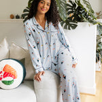 Woman wearing a sushi-themed pajama set sitting on the side of white couch in a cozy living room. ---PJ 4