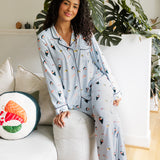 Woman wearing a sushi-themed pajama set sitting on the side of white couch in a cozy living room. ---PJ 4