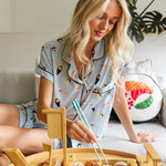 Woman in pajamas sitting on a couch with a sushi platter and chopsticks.