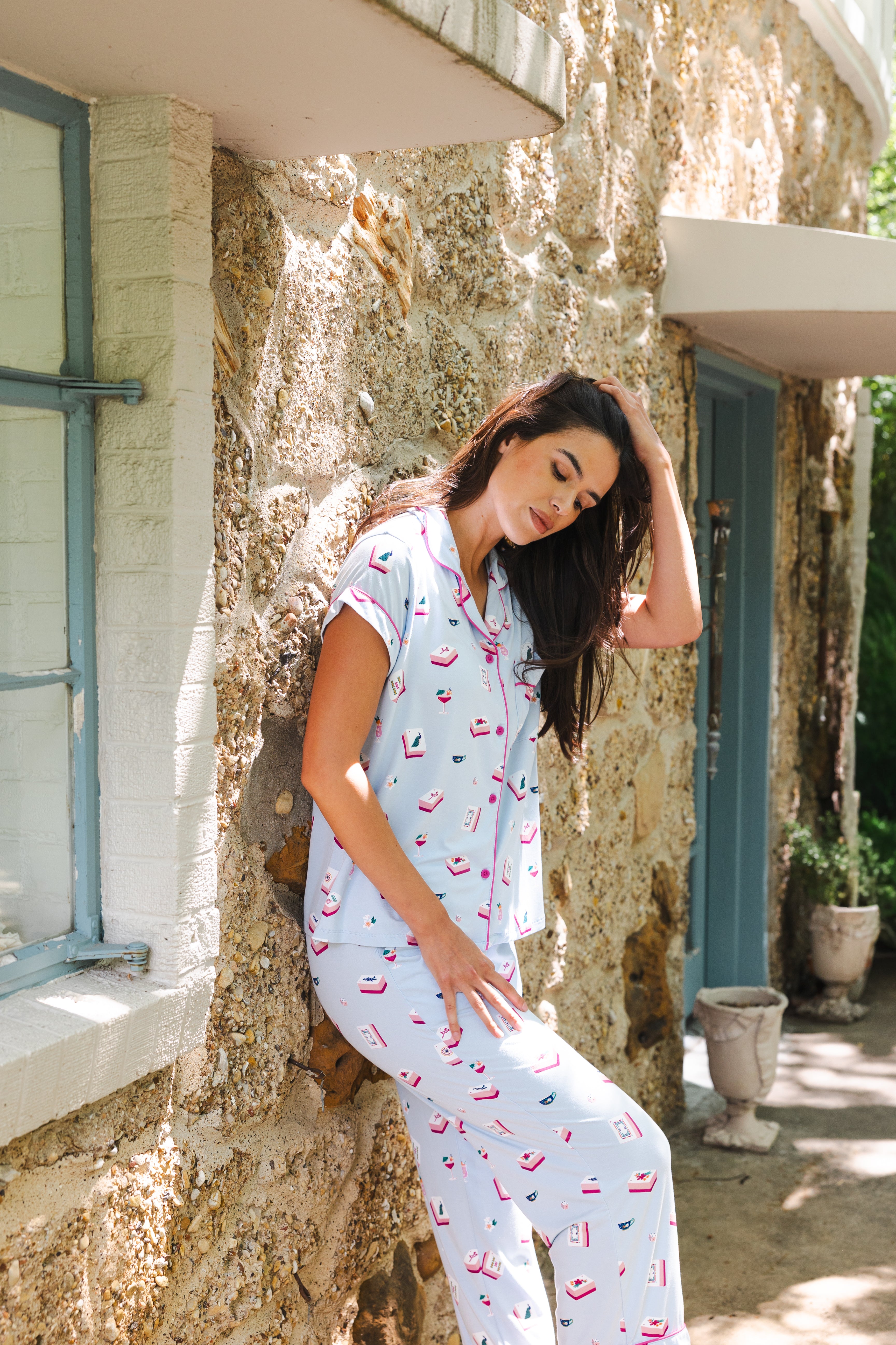Woman wearing a light blue pajama set with mahjong pattern sitting on a stone wall.