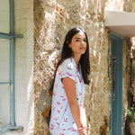 Woman in a light blue dress with pink patterns standing in front of a textured stone wall.