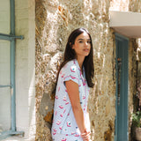 Woman in a light blue dress with pink patterns standing in front of a textured stone wall.