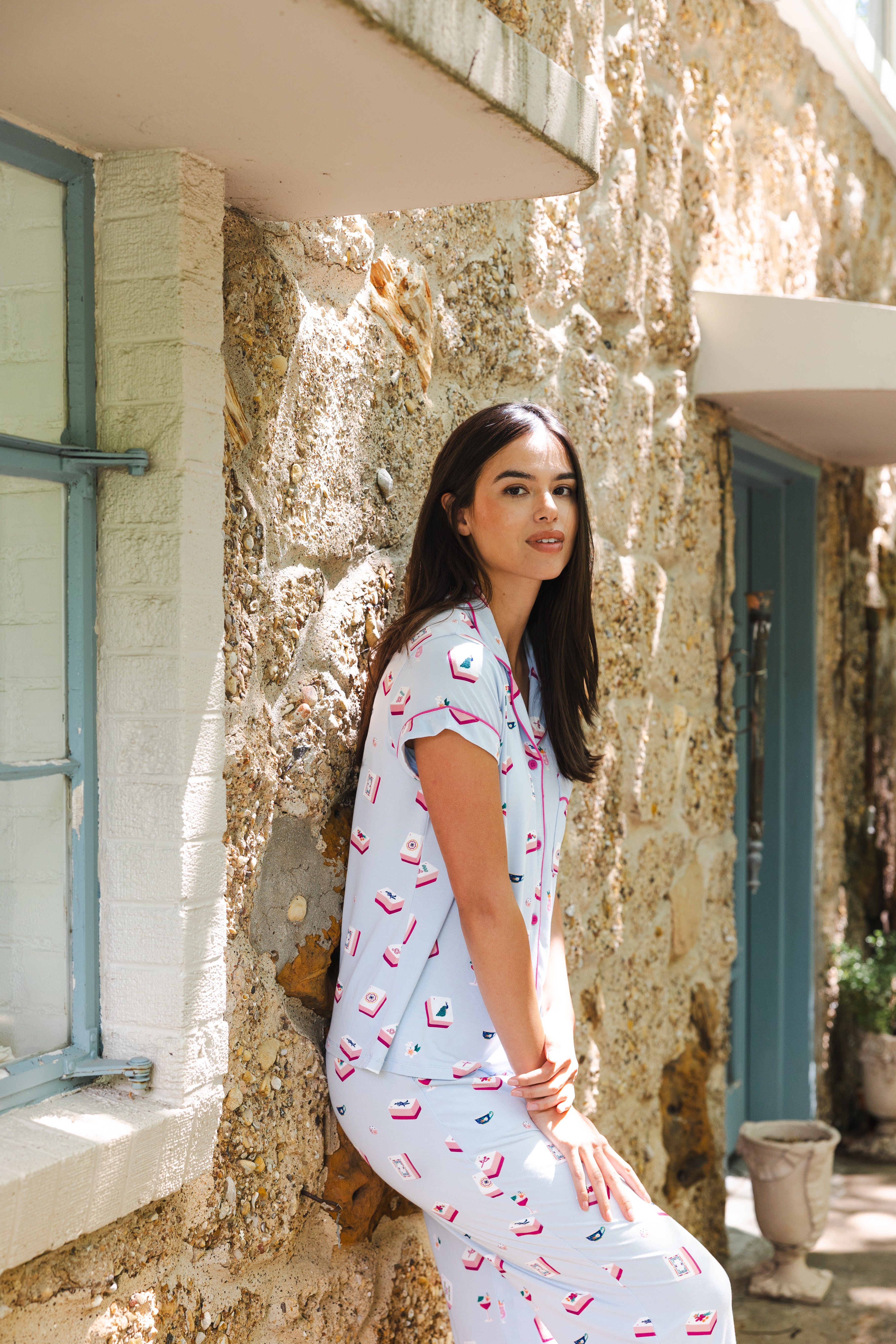 Woman in a light blue dress with pink patterns standing in front of a textured stone wall.