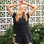 Woman in black leopard short pj set standing outdoors with greenery and a decorative wall in the background ::: Model is 5'9" wearing size XS ///