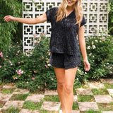 Woman in a black leopard patterned outfit standing outdoors with greenery and a decorative wall in the background