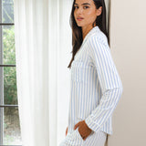 Woman wearing a blue and white striped pajama set standing by a window.