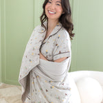 Smiling model wrapped in the Throw Blanket in Starry Icon 1.0 wearing matching short sleeve pajama set in front of a light green paneled wal 