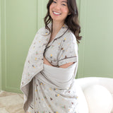 Smiling model wrapped in the Throw Blanket in Starry Icon 1.0 wearing matching short sleeve pajama set in front of a light green paneled wal 