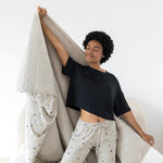 Model on knees on a bed with the Quilt Blanket in Starry Icon 2.5 stretched behind her while she wears matching lounge pants 