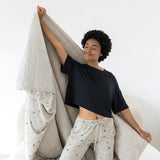 Model on knees on a bed with the Quilt Blanket in Starry Icon 2.5 stretched behind her while she wears matching lounge pants 