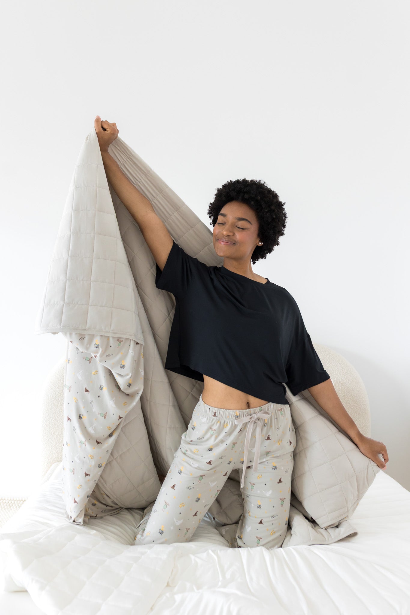 Model on knees on a bed with the Quilt Blanket in Starry Icon 2.5 stretched behind her while she wears matching lounge pants 