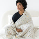 Model sitting on a bed with closed eyes and wrapped in the Quilt Blanket in Starry Icon 2.5