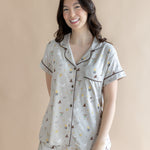 Smiling model standing infront of a beige back ground while wearing the Short Sleeve Pajama Set in Starry Icon ::: Model is 5'6" wearing size S ///