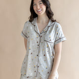 Smiling model standing infront of a beige back ground while wearing the Short Sleeve Pajama Set in Starry Icon ::: Model is 5'6" wearing size S ///