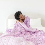 Model sitting on a white bed with Adult Blanket in Thistle Leopard print wearing similar print pajamas