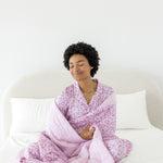 Model wrapped in Adult Blanket in Thistle Leopard print wearing similar print long sleeve pajama set on a white bed