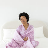Model wrapped in Adult Blanket in Thistle Leopard print wearing similar print long sleeve pajama set on a white bed
