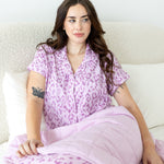 Model posing under Thistle Leopard print Throw Blanket wearing a similar print shirt on a white background