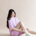 Model sitting in Women’s Biker Short Set in Thistle Leopard print with white socks and shoes on a beige background