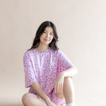 Model sitting in Women’s Biker Short Set in Thistle Leopard print with white socks and shoes on a beige background