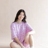 Model sitting in Women’s Biker Short Set in Thistle Leopard print with white socks and shoes on a beige background
