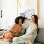 Laughing models sitting on a gray couch while wearing the Adult Sleep Bag Walker in Sage and Latte 