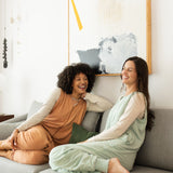 Laughing models sitting on a gray couch while wearing the Adult Sleep Bag Walker in Sage and Latte 