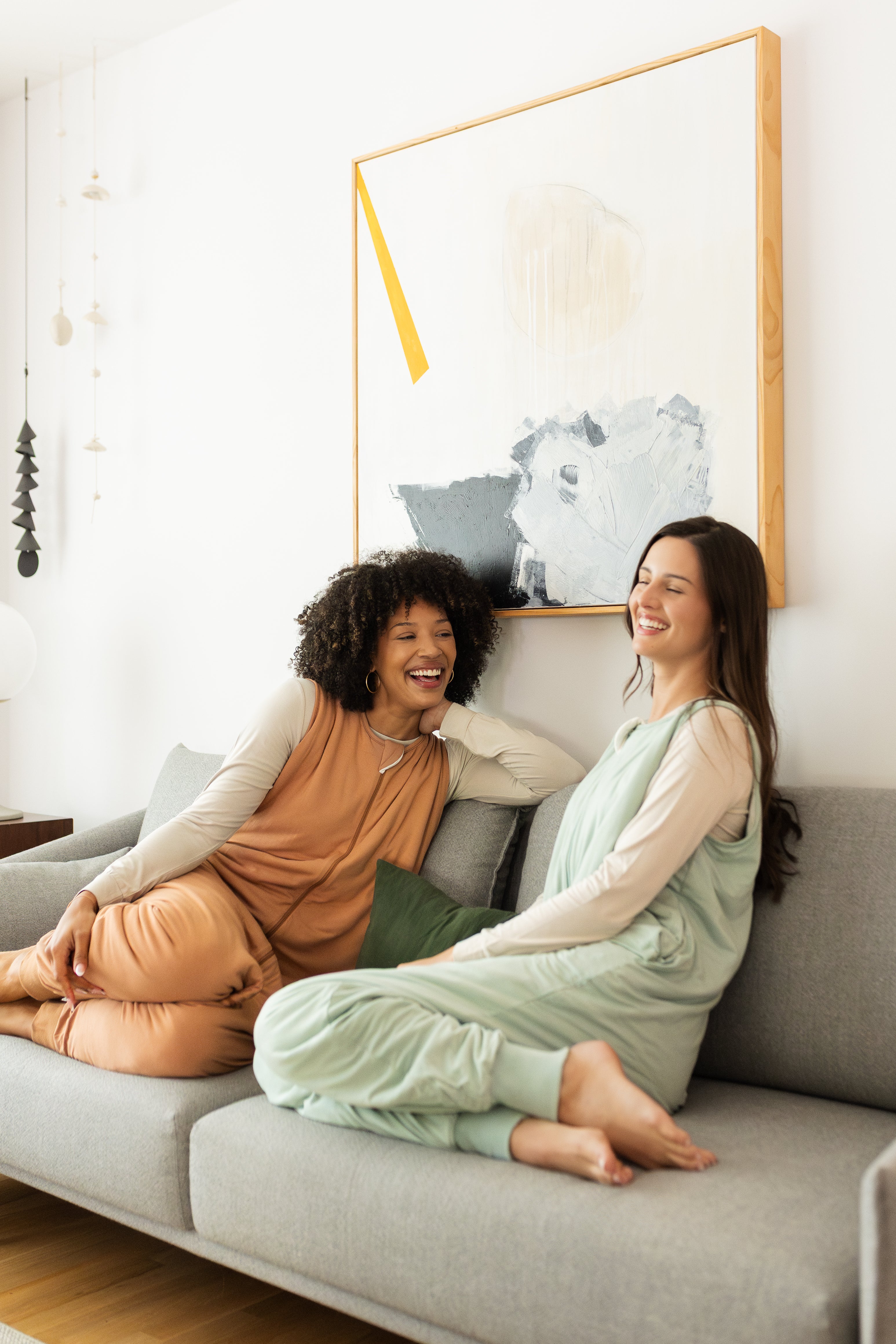 Laughing models sitting on a gray couch while wearing the Adult Sleep Bag Walker in Sage and Latte 